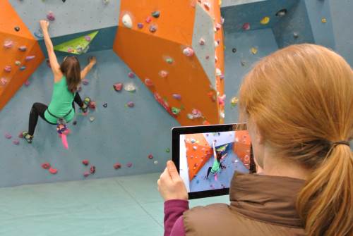 Girl in a green top being filmed bouldering by women with a tablet