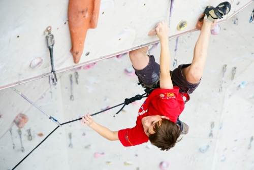 Boy lead climbing in a competition, reaching down for the rope