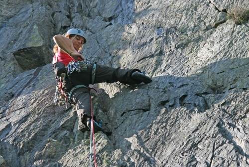 Woman reaching for gear on her harness as she climbs up a multi-pitch route